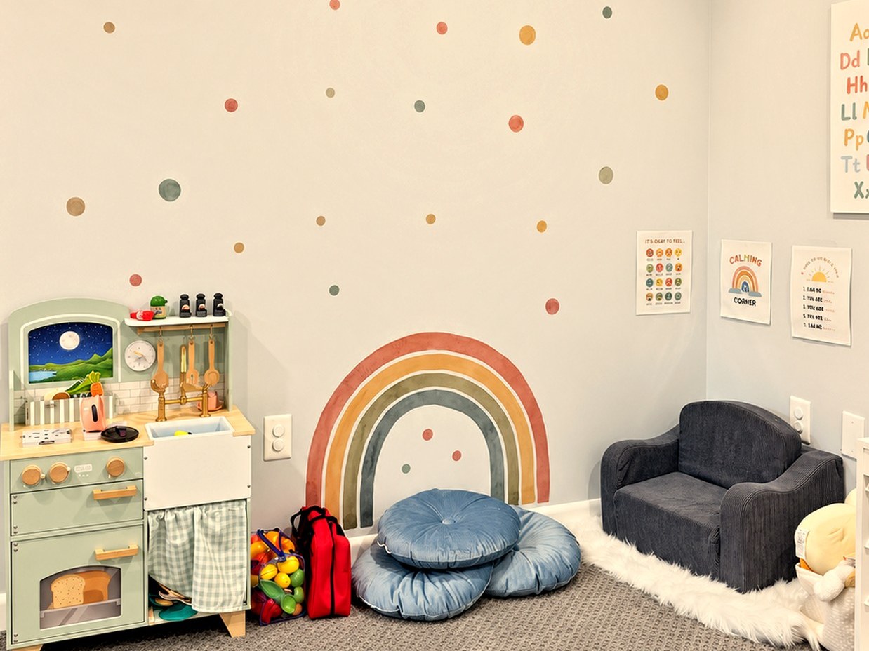 Calm corner with floor cushions, play kitchen, and calming-corner posters